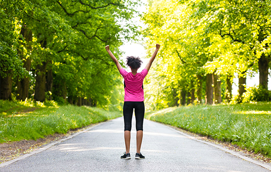 Young girl in pink and black on a wooded road reaching to the sky