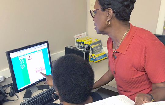 Pat Adams standing behind another woman at a computer screen showing her something